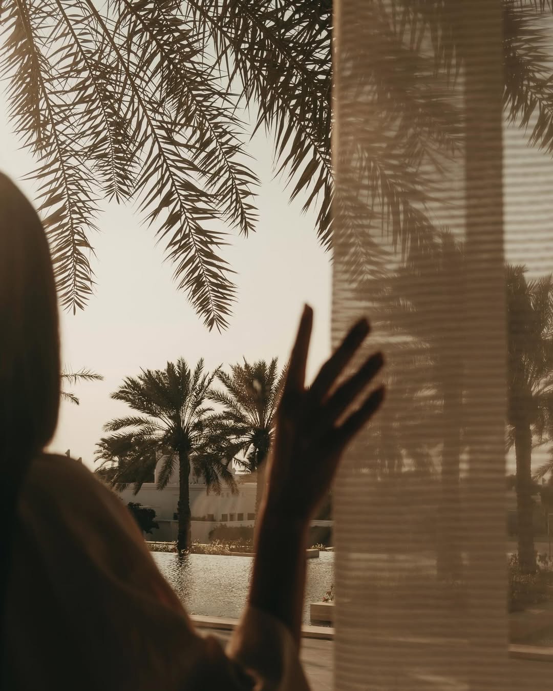 Photo of a woman thinking and talking close to a swimming pool, surrounded by palm trees
